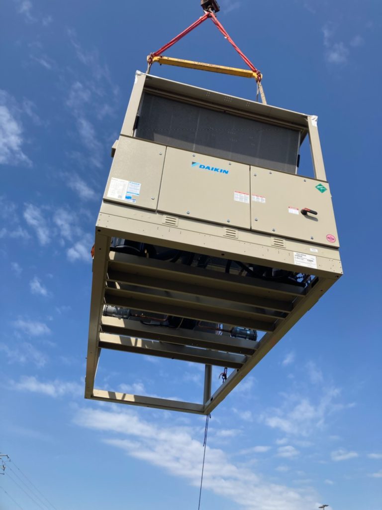 A crain holds a new commercial air conditioning unit in the air