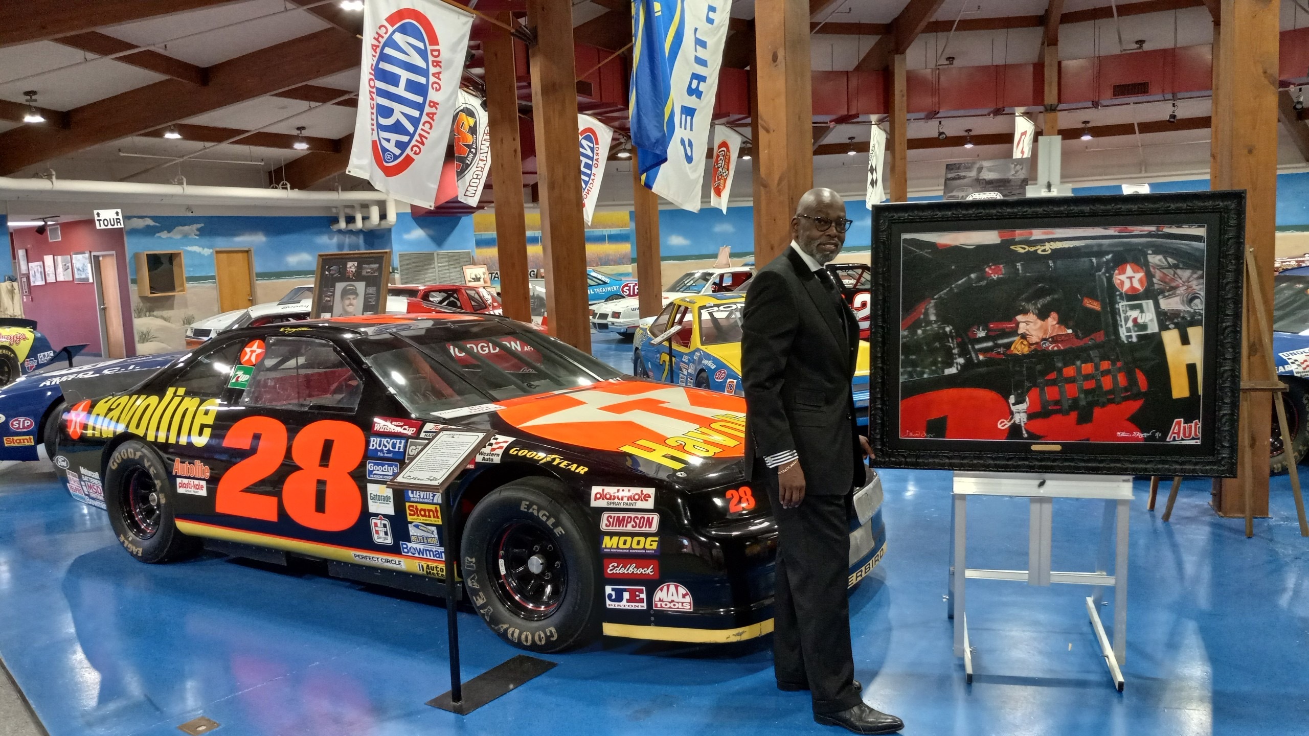 Steve Skipper standing next to his painting of Davey Allison and Davey Allison's racecar.